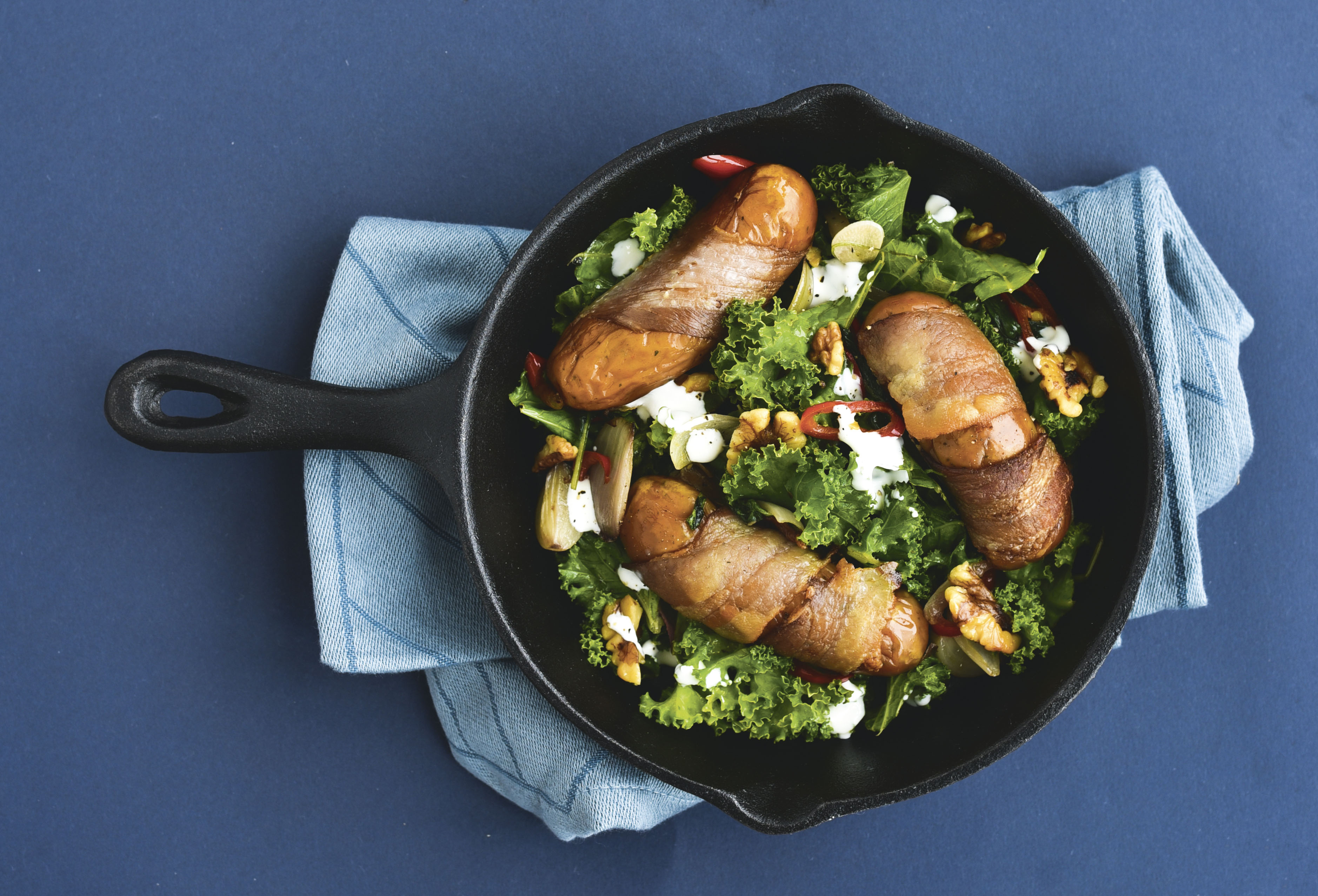 Baconsvøbte pølser og lynstegt grønkål med chili og valnødder